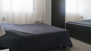 Une chambre à coucher moderne avec un lit de couleur sombre, une table de chevet, une lampe et un grand miroir.