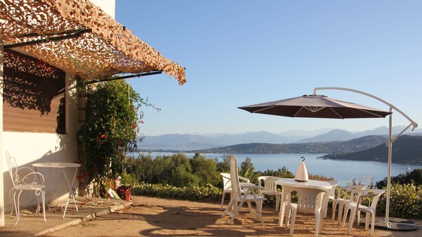 Un espace extérieur aménagé avec une table et des chaises, un parasol décoratif, et une vue sur un plan d’eau et des montagnes.