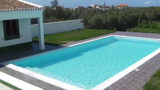A rectangular swimming pool with a tiled edge, surrounded by a paved deck.