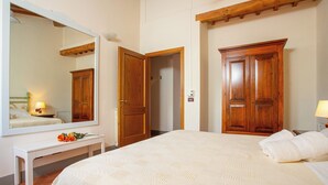 A bedroom with a large bed, wooden wardrobe, a bedside table with a lamp, and a mirror on the wall.