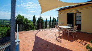 A terrace with a table and chairs, a large shade sail, and a view of the countryside.