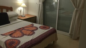 Ein Schlafzimmer mit Bett, Nachttisch, Lampe und Vorhängen.