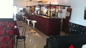 Eine Bar mit Hockern, einer Theke voller Flaschen und einem Fernsehbildschirm.
