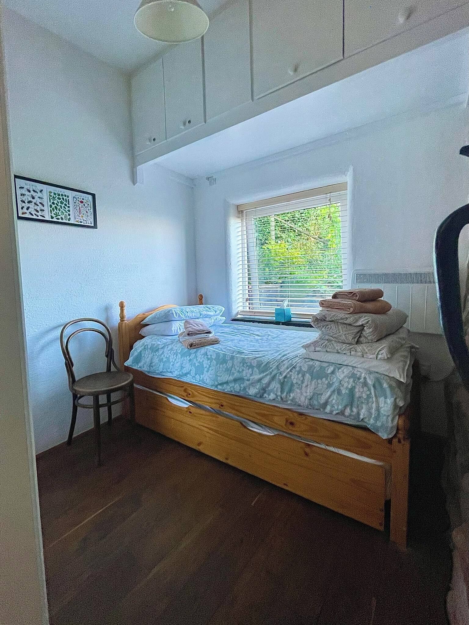 A small bedroom with a single bed, a chair, a radiator, and a window with blinds.