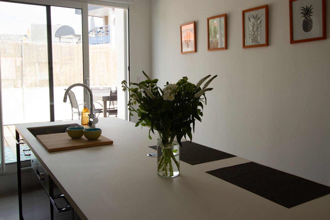 Eine Küche mit weißer Arbeitsplatte, einer Vase mit Blumen und Blick durch eine Glastür.