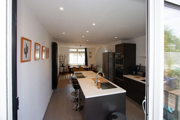 Una cocina moderna con una isla central, una zona de comedor con sillas y un refrigerador.