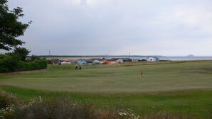 A golf course with a flagstick, houses in the background, and a body of water. - Beach Chalet With Panoramic Views (Dunbar)