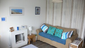 A cozy living room with a beige sofa, a fireplace, and framed pictures on the wall. - Beach Chalet With Panoramic Views (Dunbar)