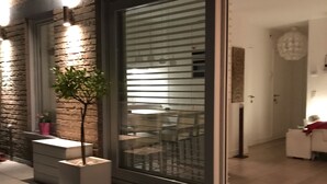 Ein modernes Gebäude mit einer großen Glasdoor, einem kleinen Baum in einem Blumentopf und einer Ziegelwand.