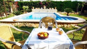 Un tavolo a bordo piscina con una ciotola di frutta, una caraffa e dei bicchieri, circondato da poltrone in vimini.