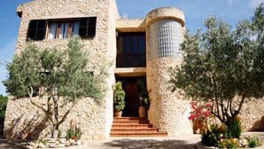 Un edificio in pietra con un ingresso centrale, scale che vi conducono e vegetazione circostante.