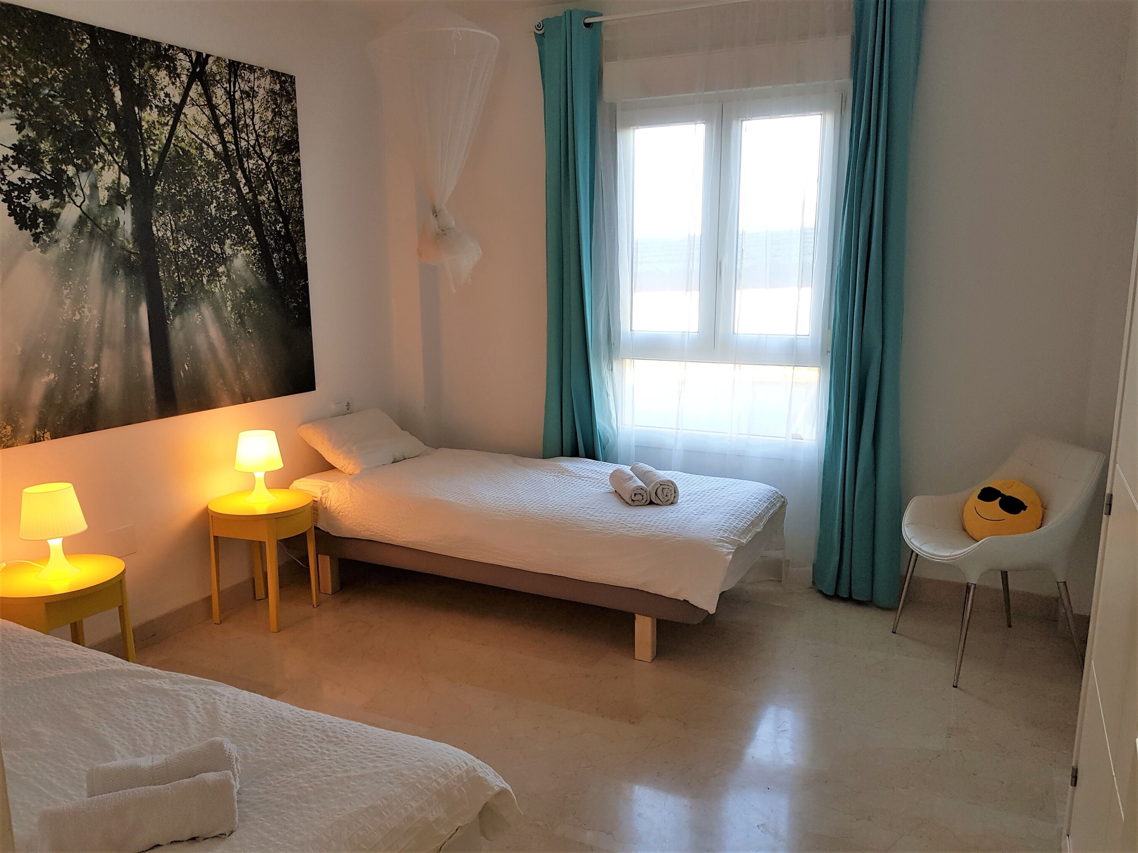 Un dormitorio con una cama, dos lámparas de noche, una ventana con cortinas, una silla y un cuadro en la pared.