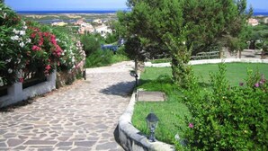 A stone pathway leading to a grassy area with a view of the sea and buildings in the distance.