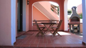 A patio with a wooden table and chairs, a brick floor, and a view of a staircase and a barbecue grill.