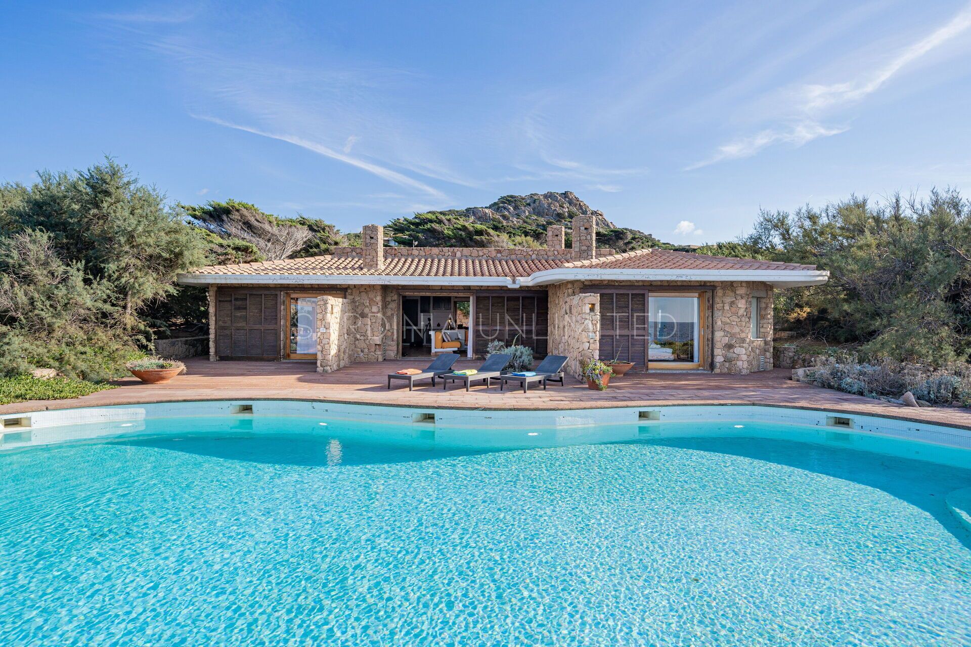 A modern house with a swimming pool, stone walls, and a patio with lounge chairs.