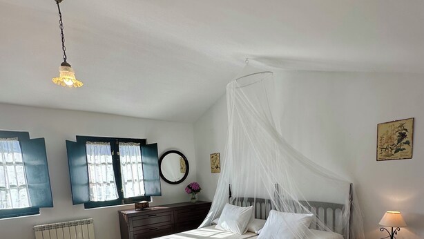 A bedroom with two beds, a bedside table with a lamp, a radiator, and a window with curtains. - Rural Accommodations Casa Fabián, La Quintana (Pet Friendly) (Castrillón)