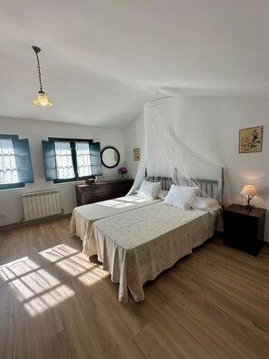 A bedroom with two beds, a bedside table with a lamp, a radiator, and a window with curtains.