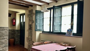 A dining area with a checkered tablecloth, wooden chairs, a stone wall, and a window with a view. - Rural Accommodations Casa Fabián, La Quintana (Pet Friendly) (Castrillón)