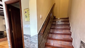 A staircase with wooden steps and a handrail, leading to a room with a tiled floor and a door. - Rural Accommodations Casa Fabián, La Quintana (Pet Friendly) (Castrillón)