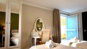 A hotel room with a bed, a vanity with a mirror, a chair, and a door leading to a balcony.