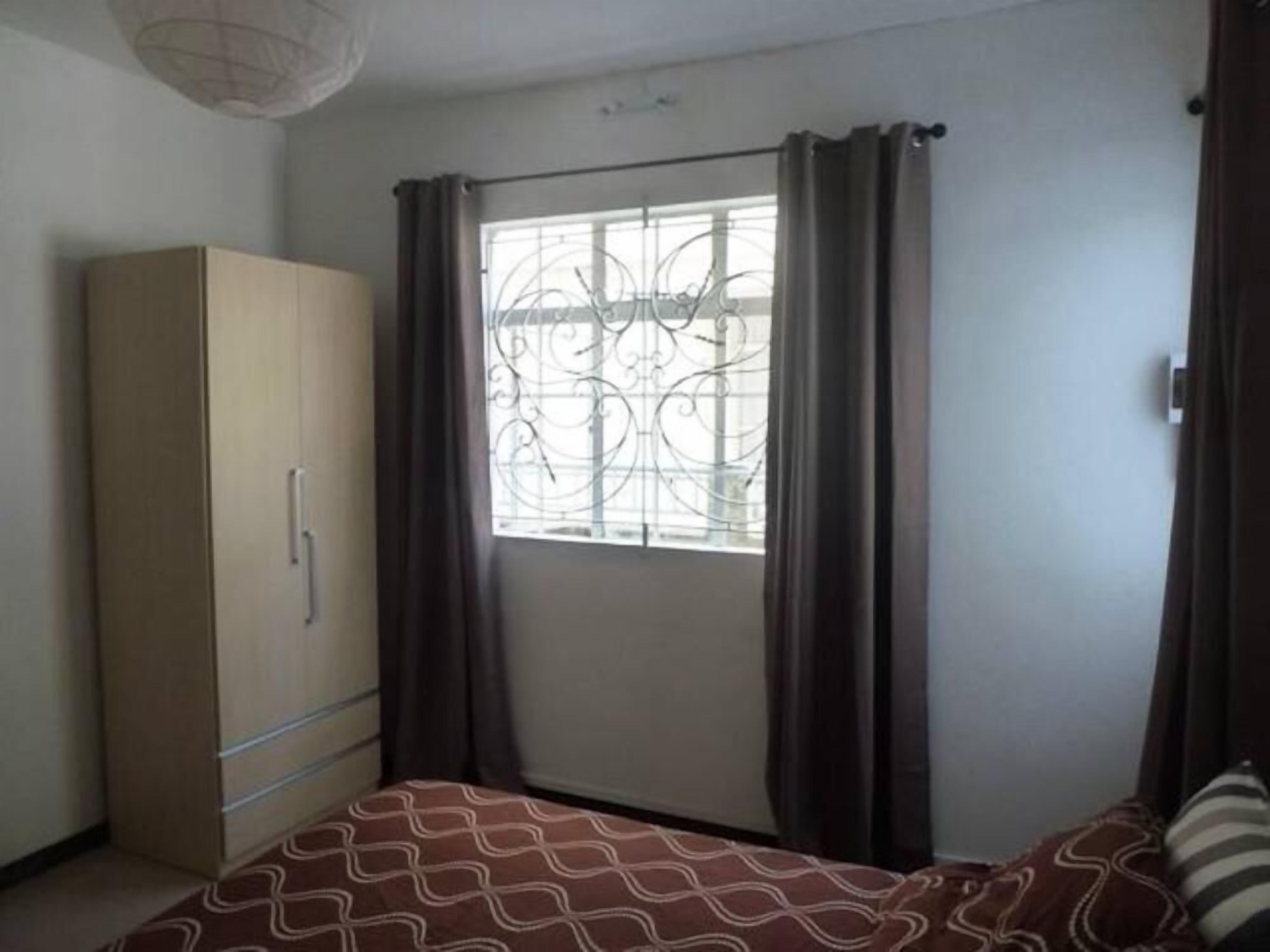A bedroom with a bed, a wardrobe, a window with curtains, and a ceiling light fixture.