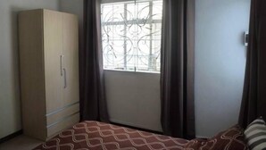 A bedroom with a bed, a wardrobe, a window with curtains, and a ceiling light fixture.