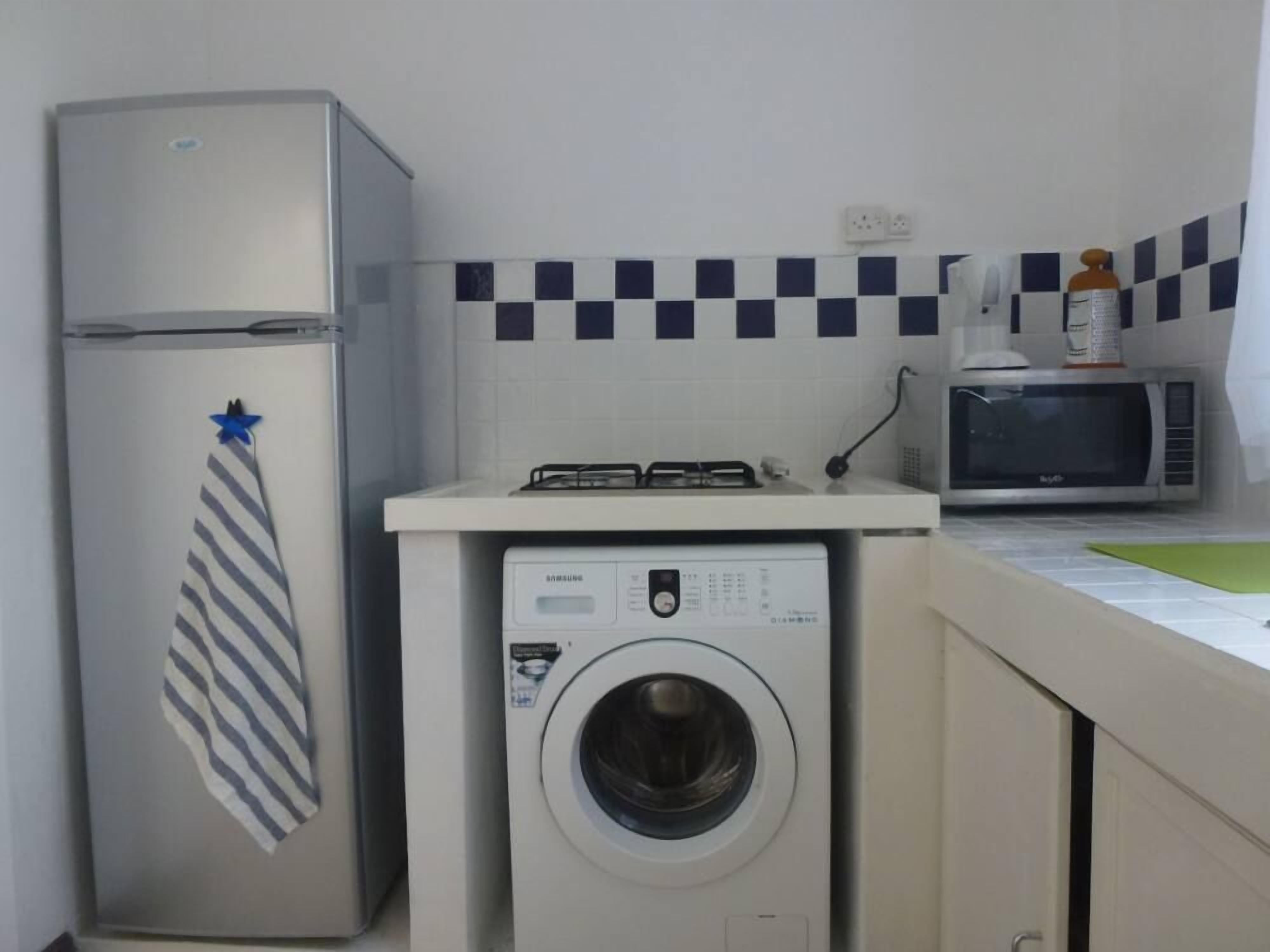 Une cuisine compacte équipée d’un réfrigérateur, d’un four à micro-ondes et d’un lave-linge.