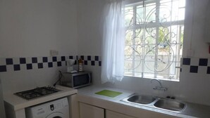 A compact kitchen with a gas stove, microwave, and washing machine, a sink, and a window with a metal grill.