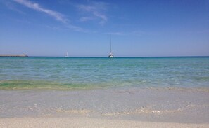 A beach with clear turquoise water, a sandy shore, and a distant sailboat. - Apartment in a villa with private parking, 5 minutes from the beaches and downtown (L'île-Rousse)