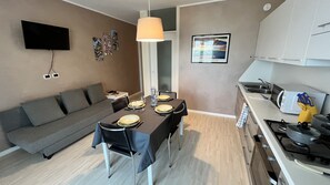 Una cucina moderna con zona pranzo, una TV a schermo piatto montata a parete e un divano nella zona soggiorno.