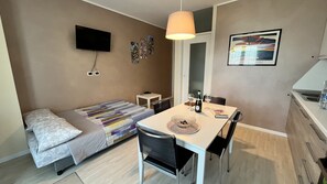 Una camera compatta con un letto, un tavolo da pranzo con sedie, una TV a parete e un angolo cottura.