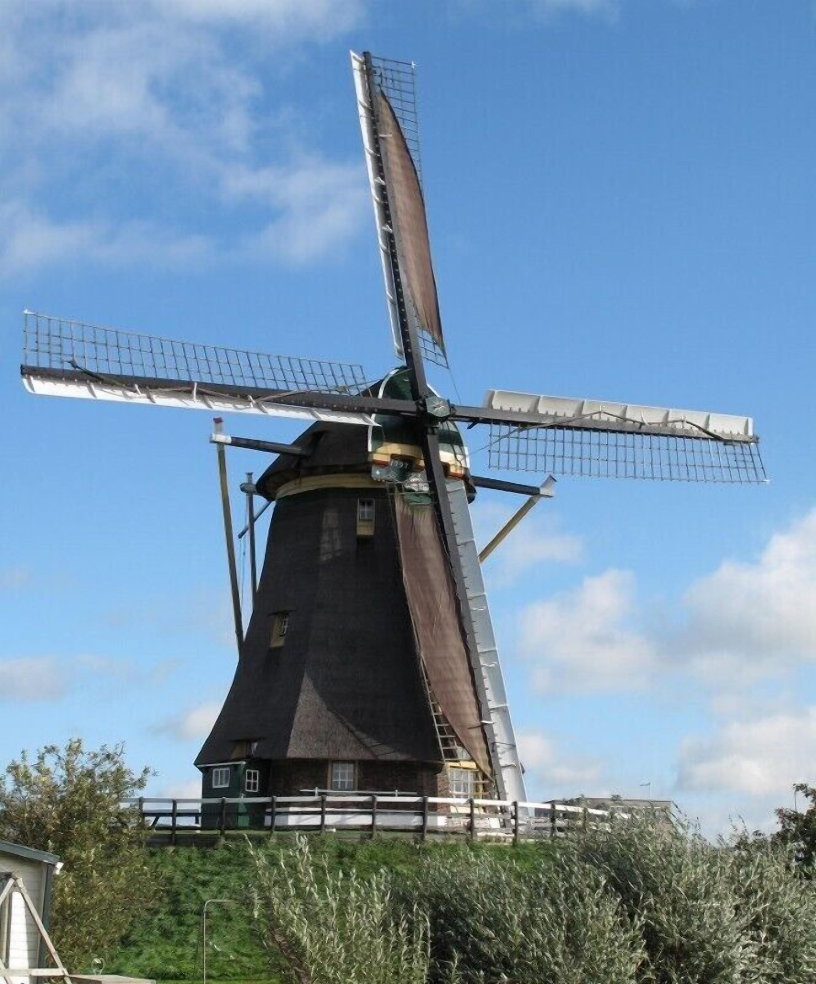 A traditional windmill with a dark, conical tower and three large sails.