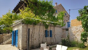 A stone building with blue shutters, a wooden pergola, and outdoor seating.