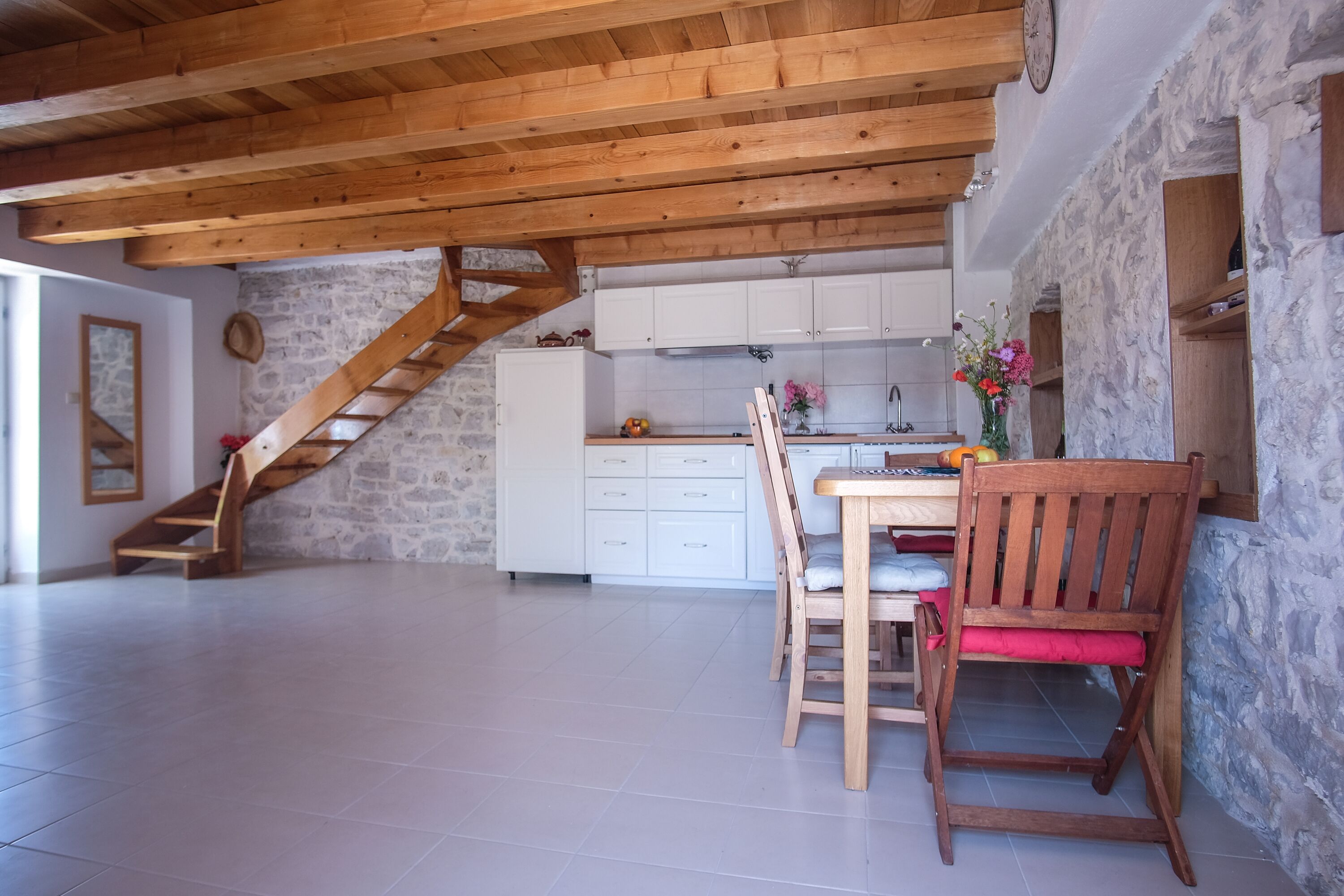 Une cuisine spacieuse avec des meubles blancs, un escalier en bois et un coin repas comprenant une table et des chaises en bois.