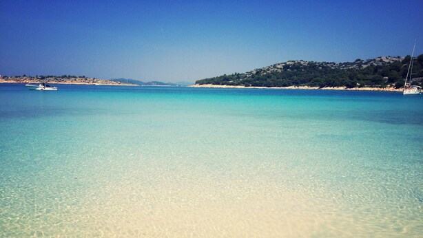 A clear beach with shallow waters and a boat in the distance.
