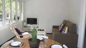 A dining area with a table set for two, a television on a stand, and a sofa with cushions. - Apartment overlooking the Sagrada Familia, completely renovated and bright (Barcelona)
