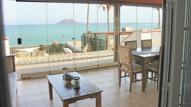 A room with a large glass door leading to a balcony overlooking the sea, a wooden table, and a chair. - Private, independent villa on the front line, terrace and tranquility (Corralejo)