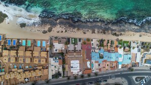 An aerial view of a coastal resort with multiple buildings, a beach, and a road with cars. - Private, independent villa on the front line, terrace and tranquility (Corralejo)