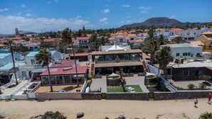 A coastal residential area with a prominent two-story house featuring a rooftop terrace, a swimming pool, and a landscaped garden. - Private, independent villa on the front line, terrace and tranquility (Corralejo)