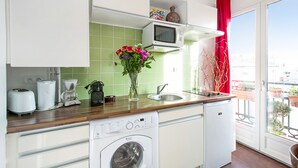 Une cuisine compacte équipée d’un lave-linge, d’un four à micro-ondes et d’un évier. Une fenêtre offre une vue sur l’extérieur.