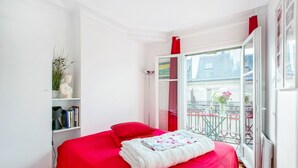 Une chambre à coucher avec une couvre-lit rouge, un oreiller blanc et une fenêtre donnant sur un balcon.