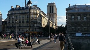 Un pont piétonnier avec des bancs, une tour et des bâtiments en arrière-plan.