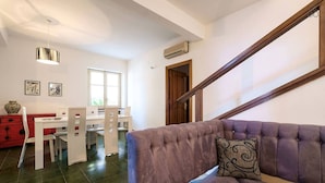 Una sala de estar con un sofá morado, una mesa de comedor con sillas y una escalera.