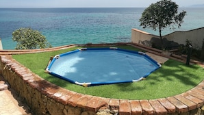 Una piscina con vista al mar, rodeada por un muro de ladrillo y césped verde.