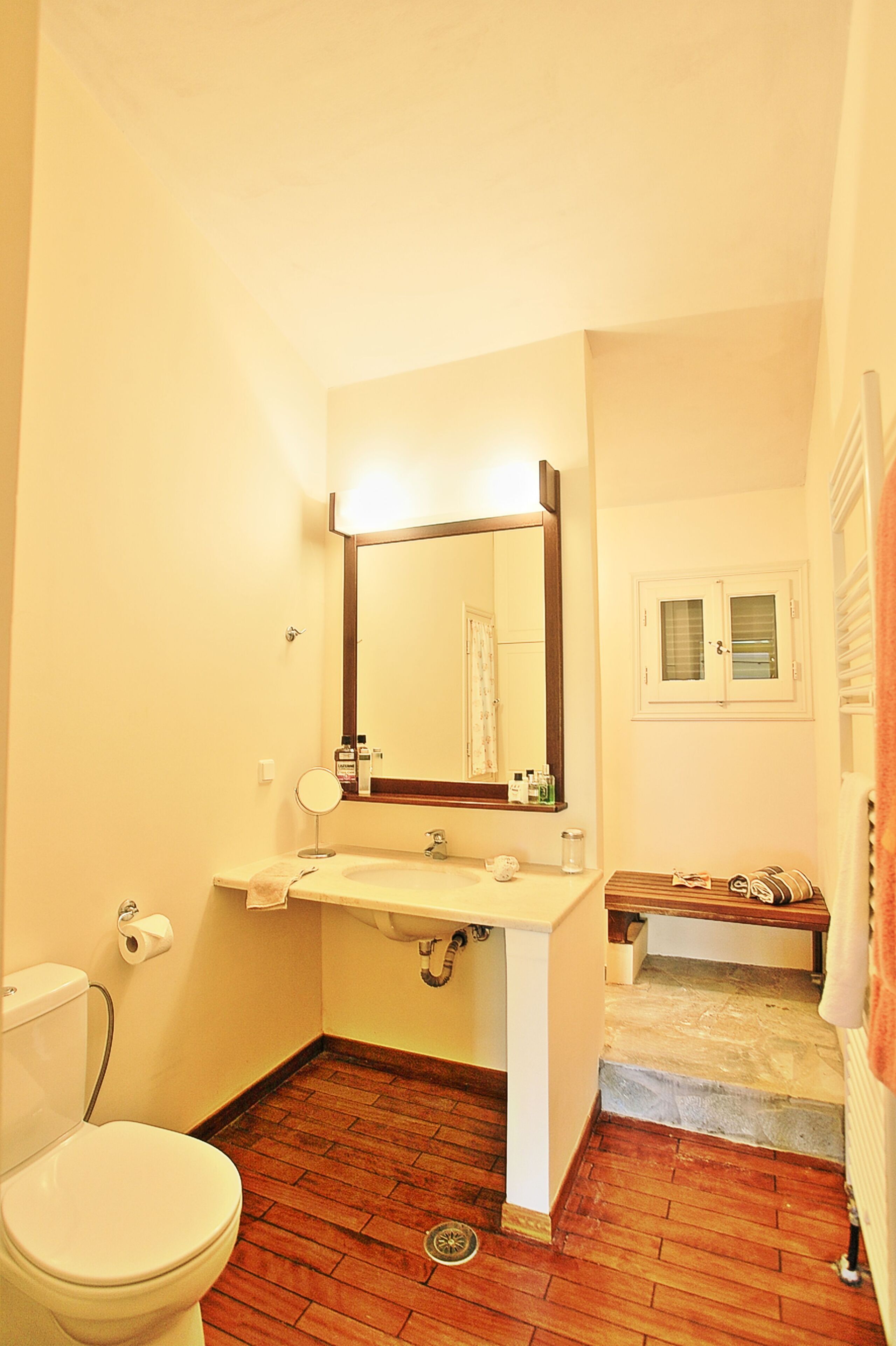 Un baño con inodoro, lavamanos, espejo y una pequeña ventana.