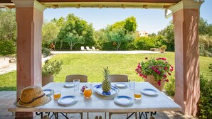 Un área de comedor al aire libre con una mesa preparada para dos personas, rodeada de vegetación y vistas a un jardín y árboles.
