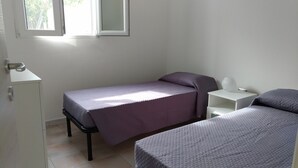 A small, clean room with two beds, a white nightstand, and a cabinet.