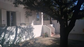 A white house with a balcony, a tree, and a small garden area.