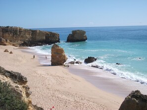 Una playa con aguas azules cristalinas, grandes formaciones rocosas y una orilla arenosa.
