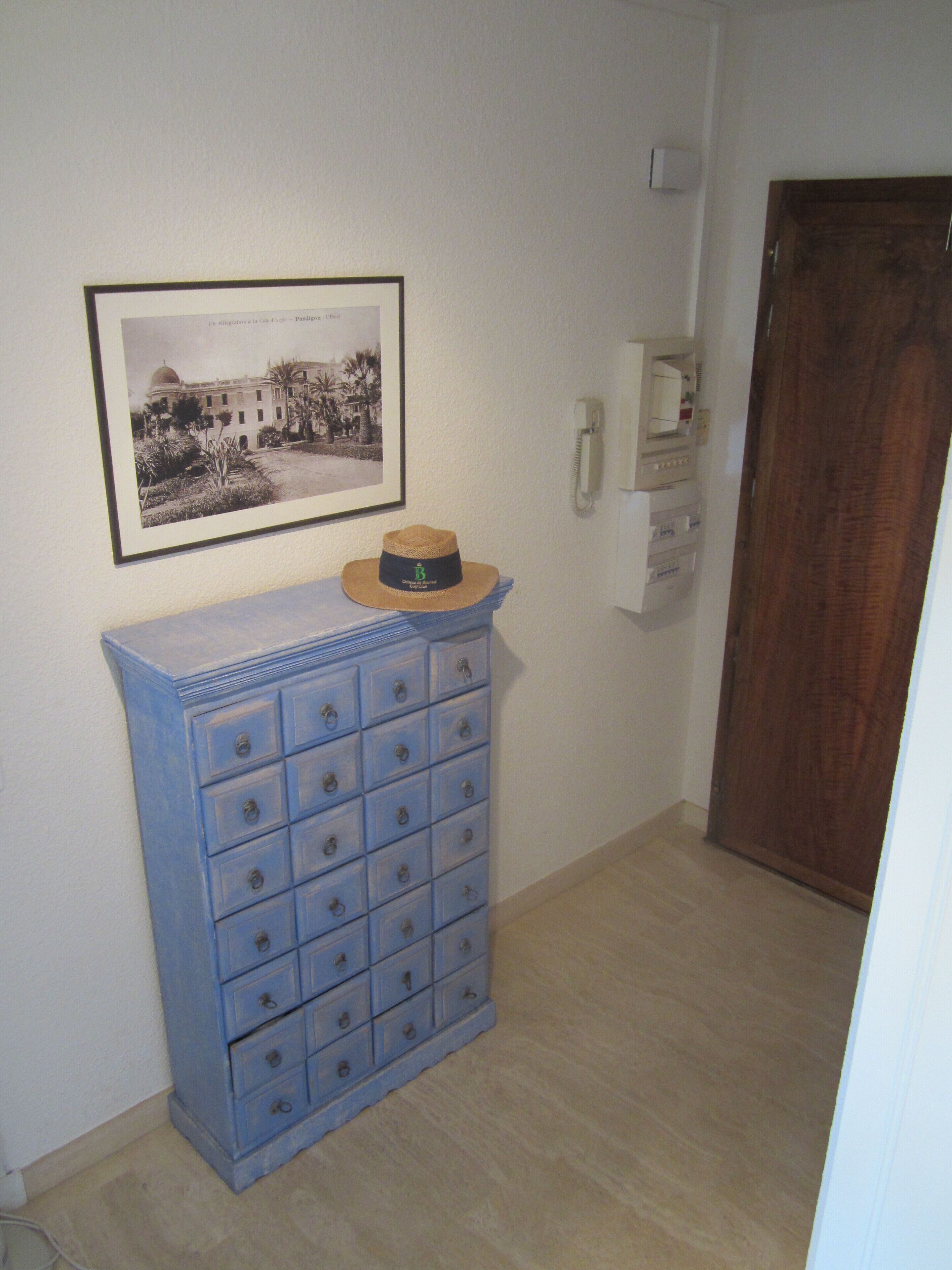 Ein Flur mit einer blauen Kommode, einem gerahmten Foto an der Wand, einem Telefon und einer Holztür.